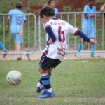 fundamentos do futebol infantil com criança dominando a bola em campo