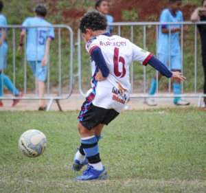 fundamentos do futebol infantil com criança dominando a bola em campo