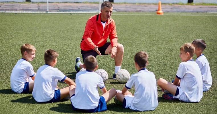 Treinador orientando crianças no futebol infantil com foco em inteligência emocional