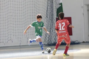 Menino sub-12 praticando passadas firmes no futsal, aprimorando equilíbrio e velocidade defensiva na quadra.