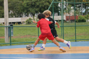 Crianças praticando futsal infantil em quadra, desenvolvendo fundamentos do futebol com foco no toque de bola e na tomada de decisão